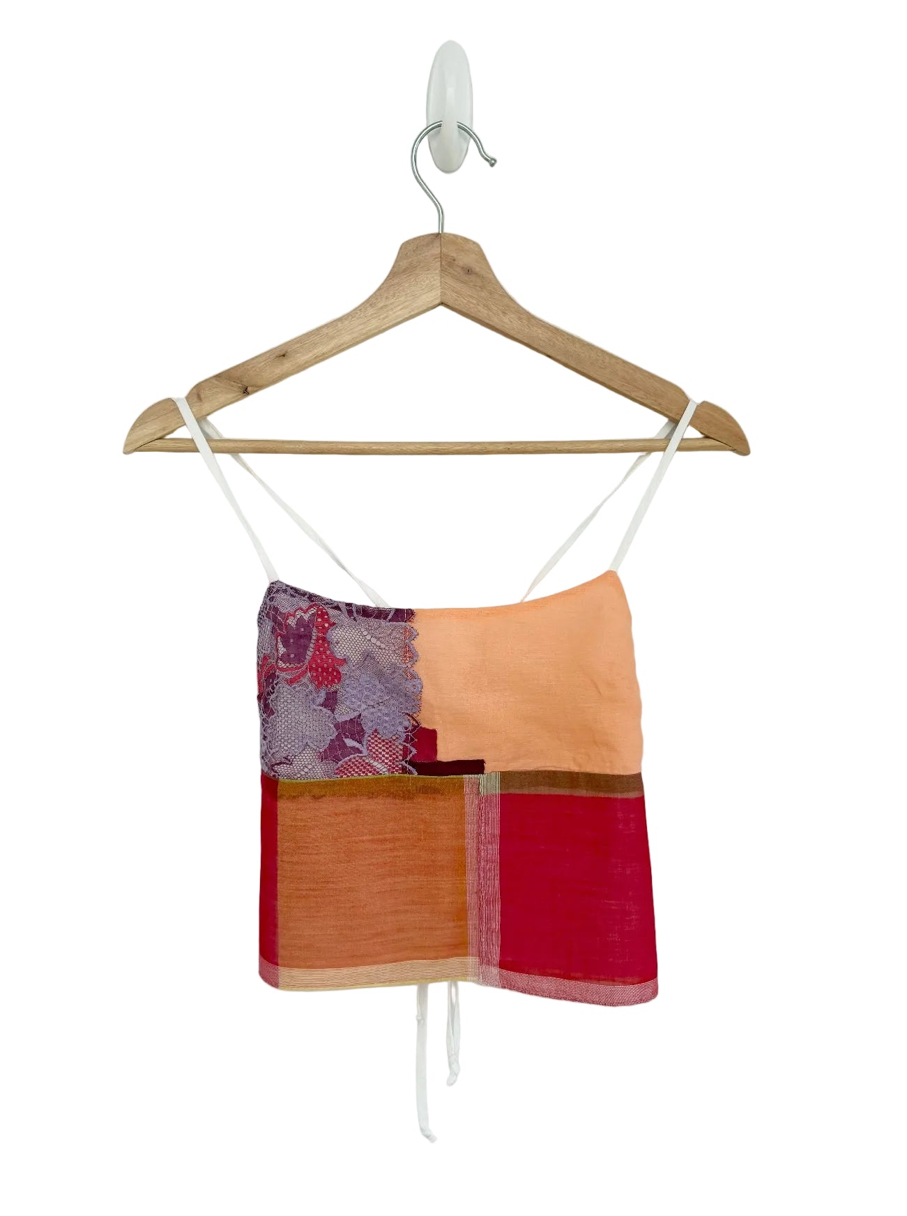 Colorful top with patchwork design on a wooden hanger against a white background