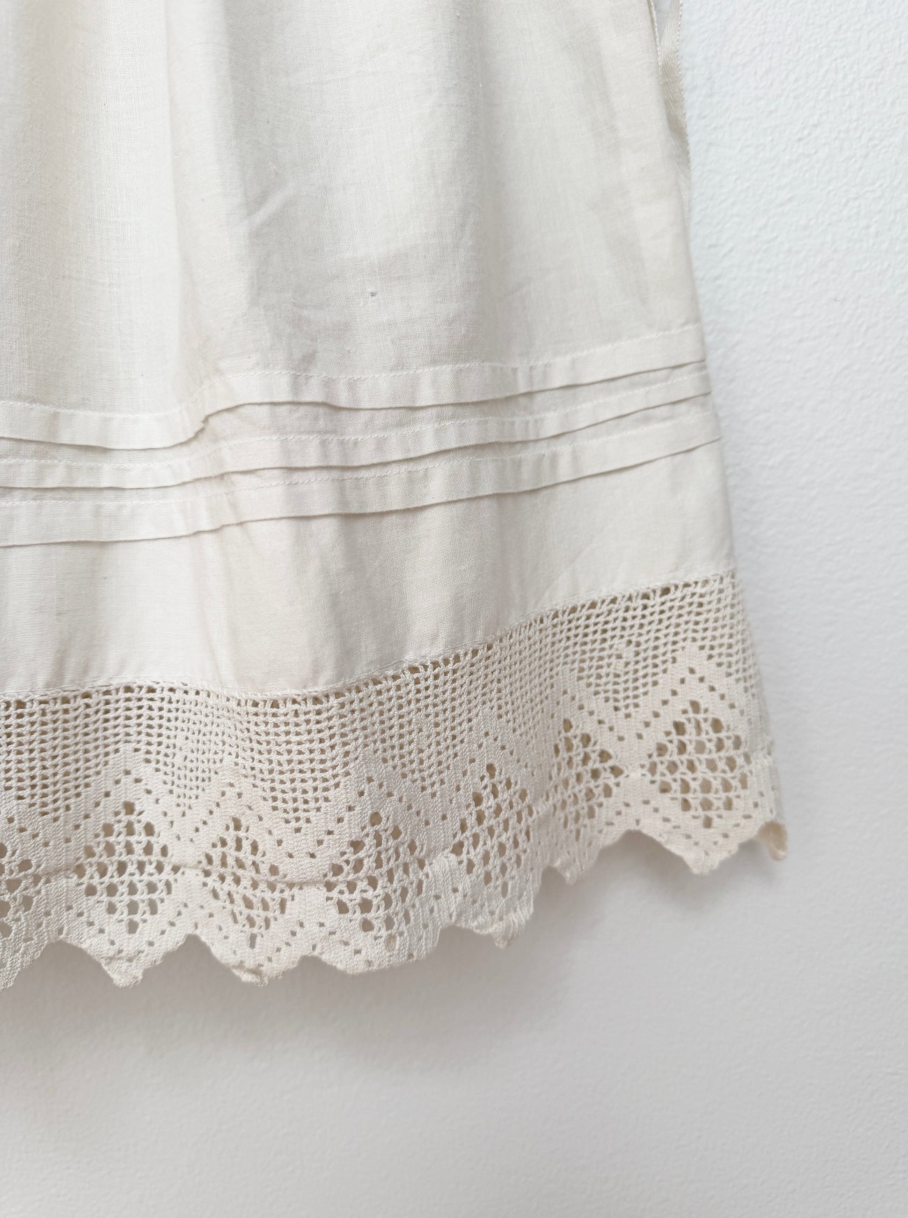 Close-up of a cream-colored fabric garment featuring a decorative scalloped crochet lace hem and horizontal stitched detailing.
