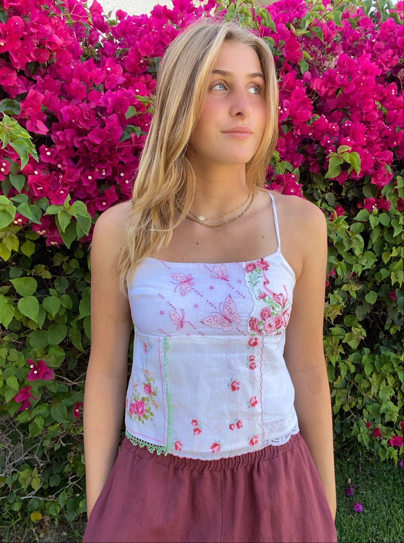 Woman wearing a floral top and maroon skirt standing in front of pink flowers