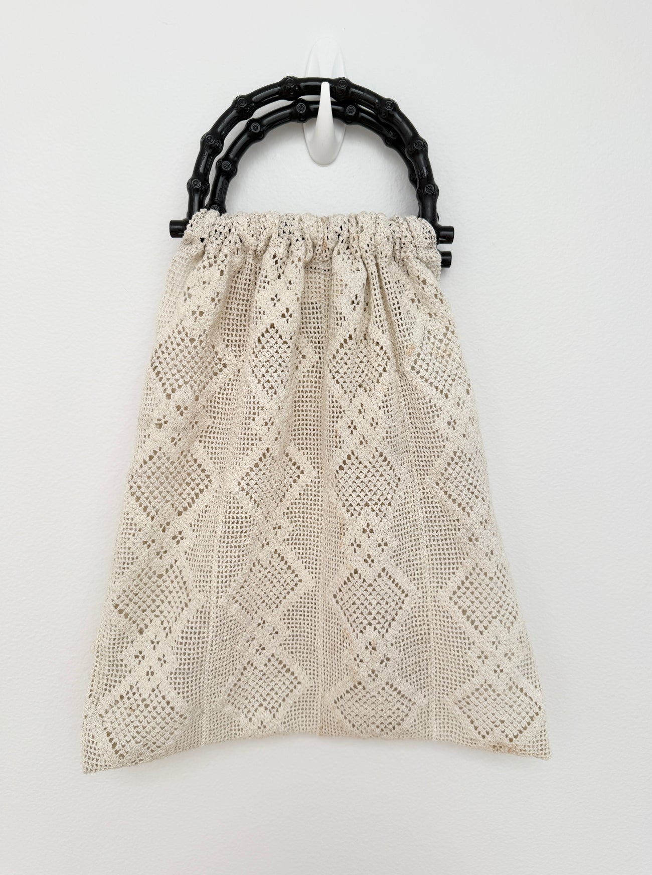 A cream-colored crochet handbag with a geometric openwork pattern, featuring a black bamboo-style top handle, shown against a plain white background.