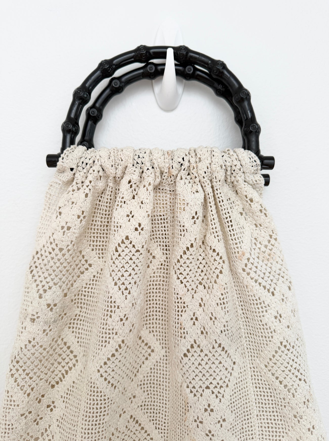 A cream-colored crochet handbag with a textured diamond pattern, featuring a black bamboo-style top handle.