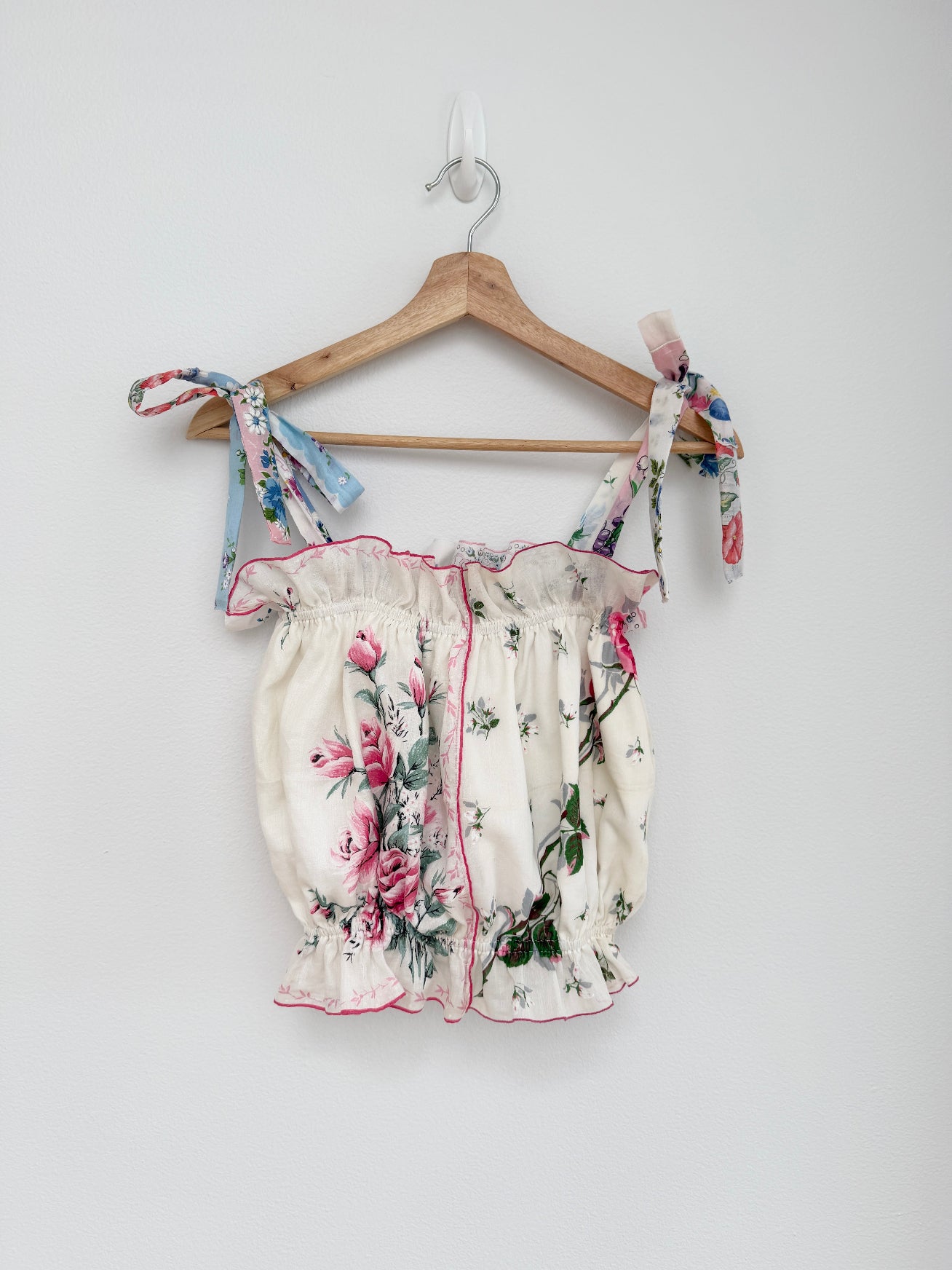 Floral top with ruffled details on a hanger against a white background